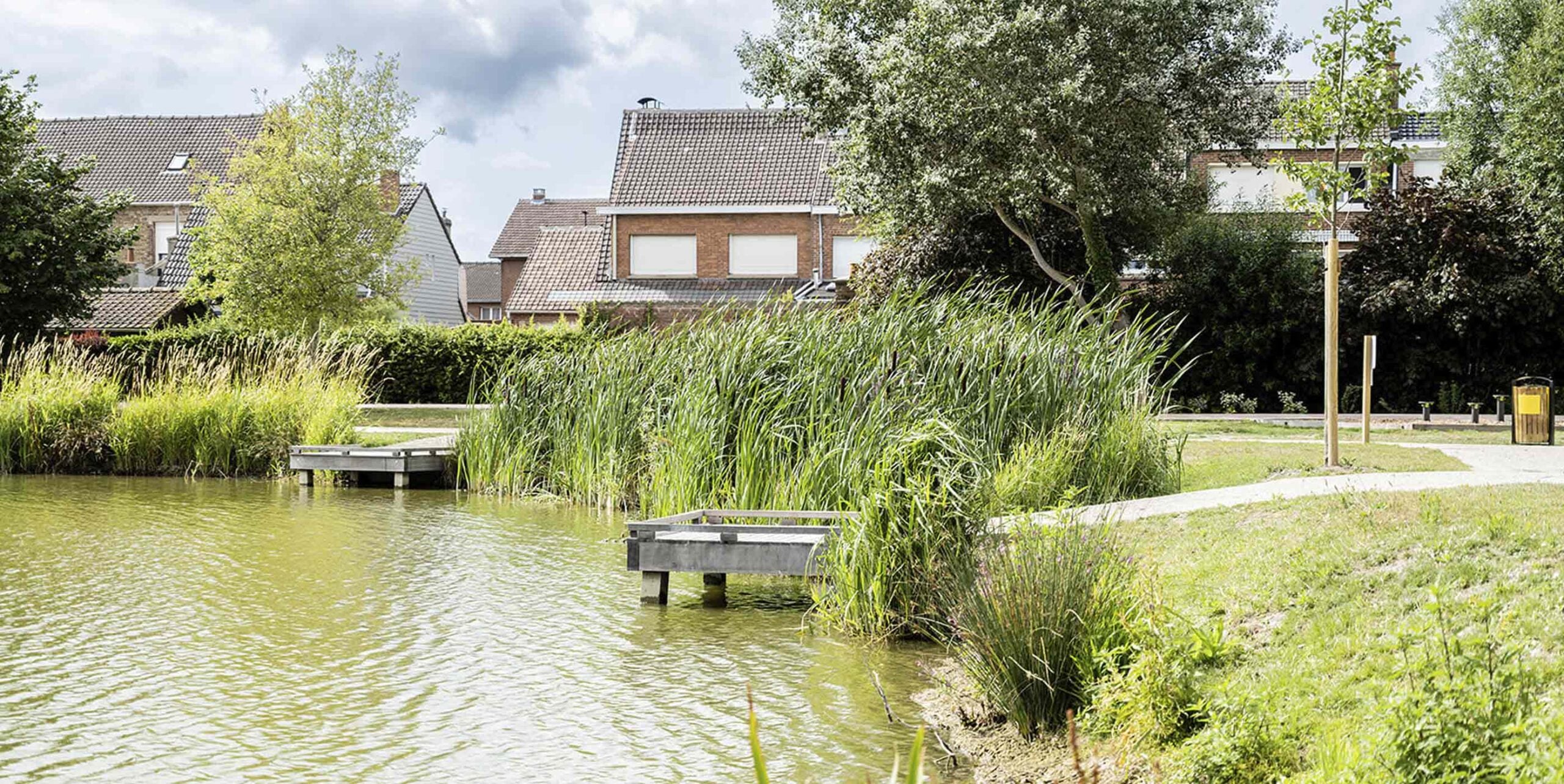 Teich mit Schilf und Holzstegen im Wohngebiet, gepflegte Grünanlage mit Wegen und Bäumen