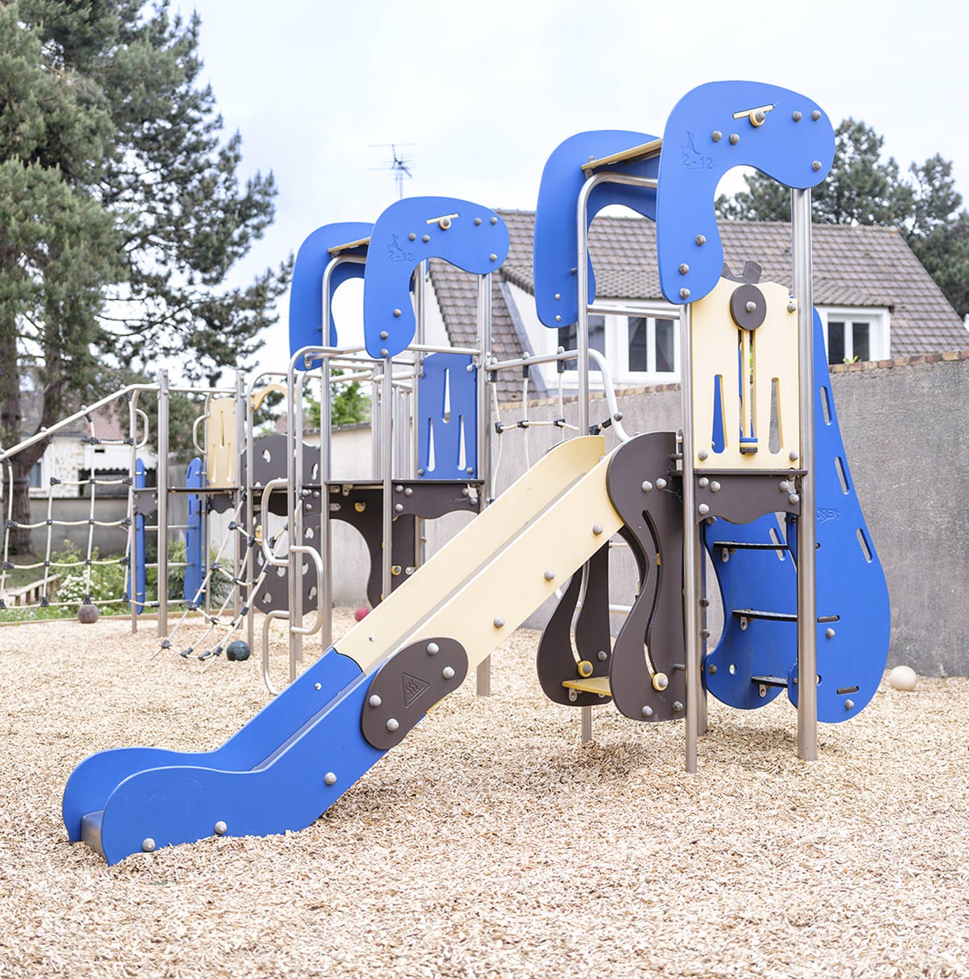 Spielplatz mit blauer Rutsche und Klettergerüst auf Rindenmulch, im Hintergrund Wohnhäuser