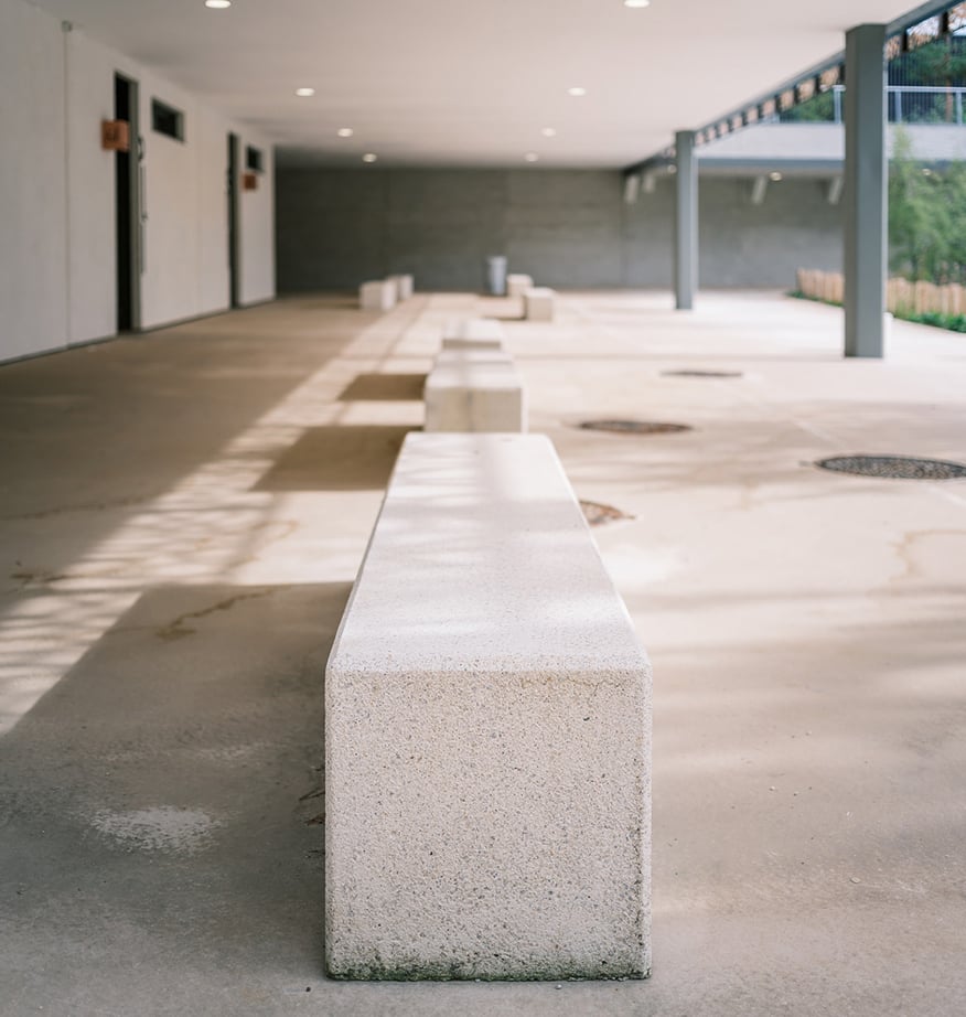 Betonsitzbänke im Außenbereich eines Gebäudes mit überdachtem Gang und gepflasterter Fläche