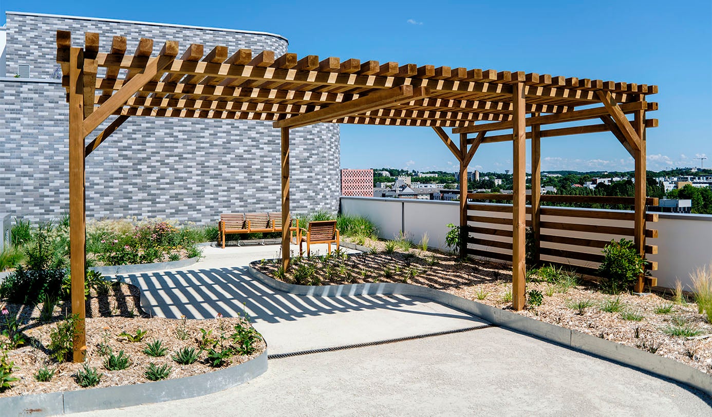 Dachterrasse mit Holzpergola, Sitzbank und pflegeleichter Bepflanzung vor urbaner Skyline