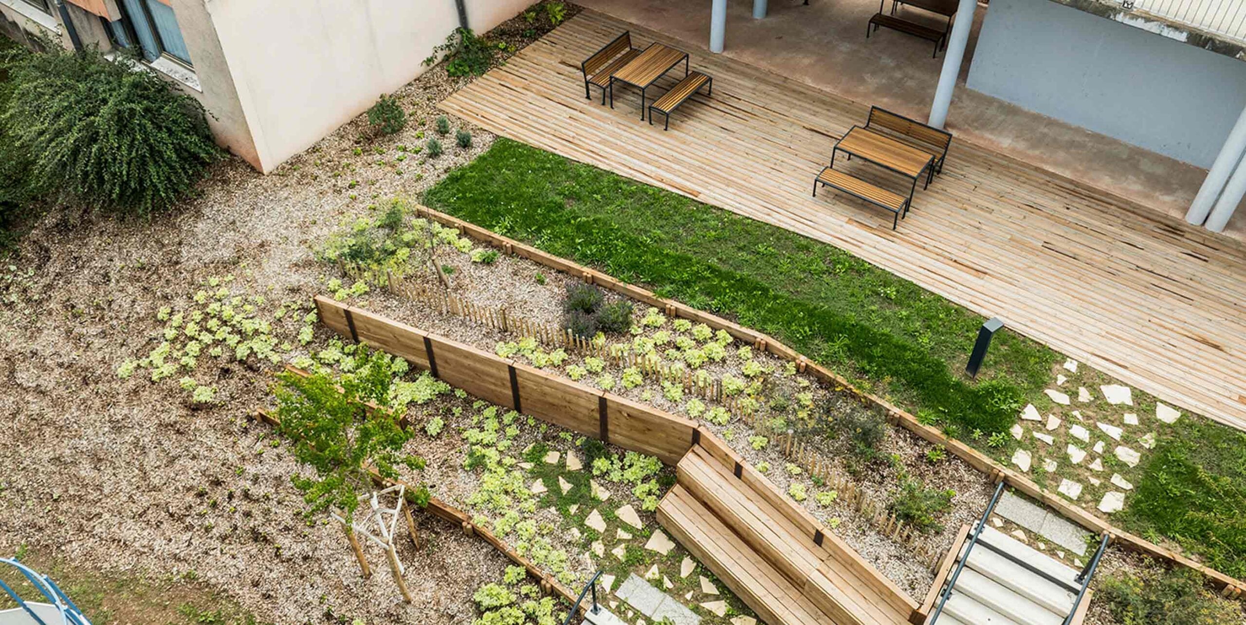 Luftaufnahme einer begrünten Innenhofgestaltung mit Holzterrasse, Sitzbänken, Rasenfläche und Staudenbeeten