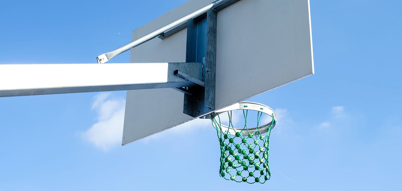 Basketballkorb mit grünem Netz und Metallbefestigung am Backboard vor blauem Himmel