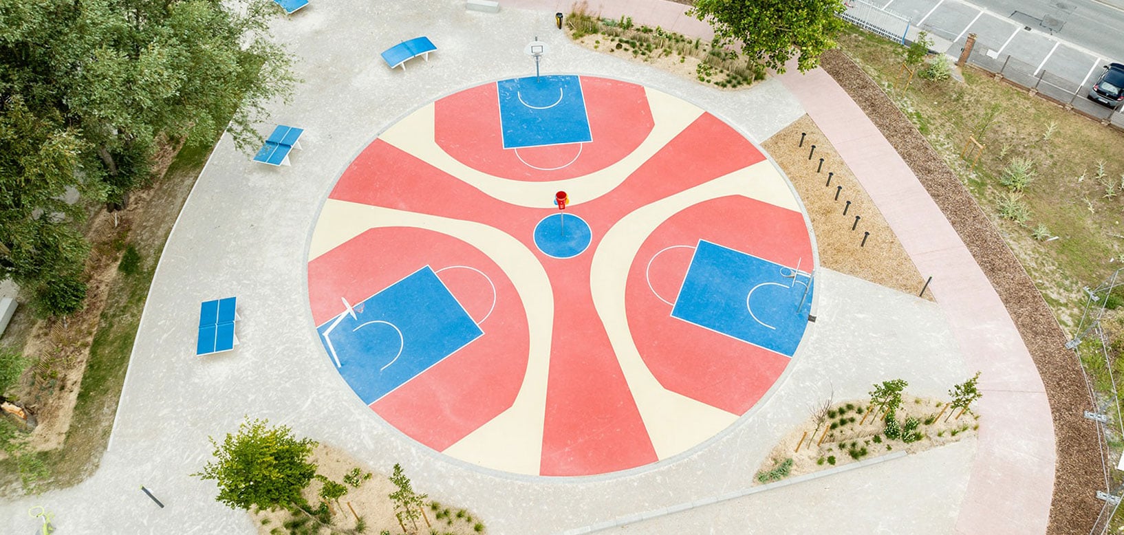 Kreisförmiger Multisport-Platz mit drei Basketballfeldern, Tischtennisplatten und Grünanlagen aus der Vogelperspektive