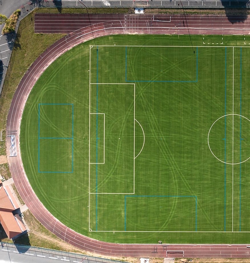 Luftaufnahme eines gepflegten Sportplatzes mit Rasenspielfeld, Laufbahn und markierten Trainingszonen