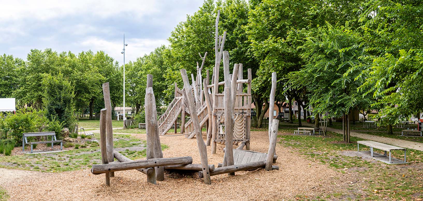 Naturspielplatz aus Robinienholz mit Rutsche und Kletterelementen im Park, umgeben von Bäumen