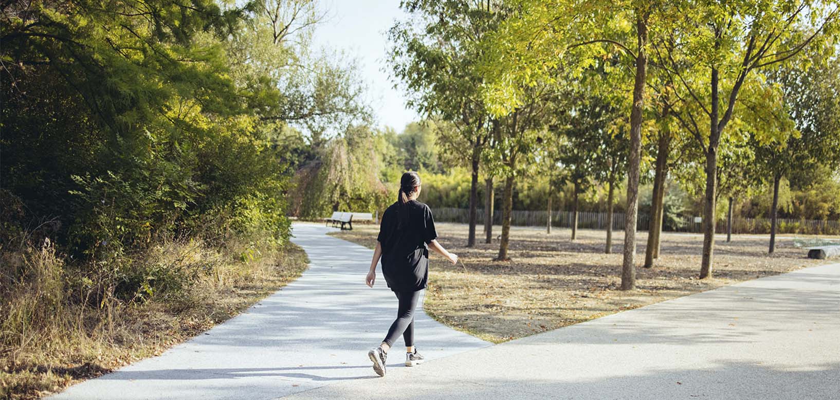 Frau joggt auf asphaltiertem Weg durch gepflegte Parkanlage mit Bäumen und Grünflächen